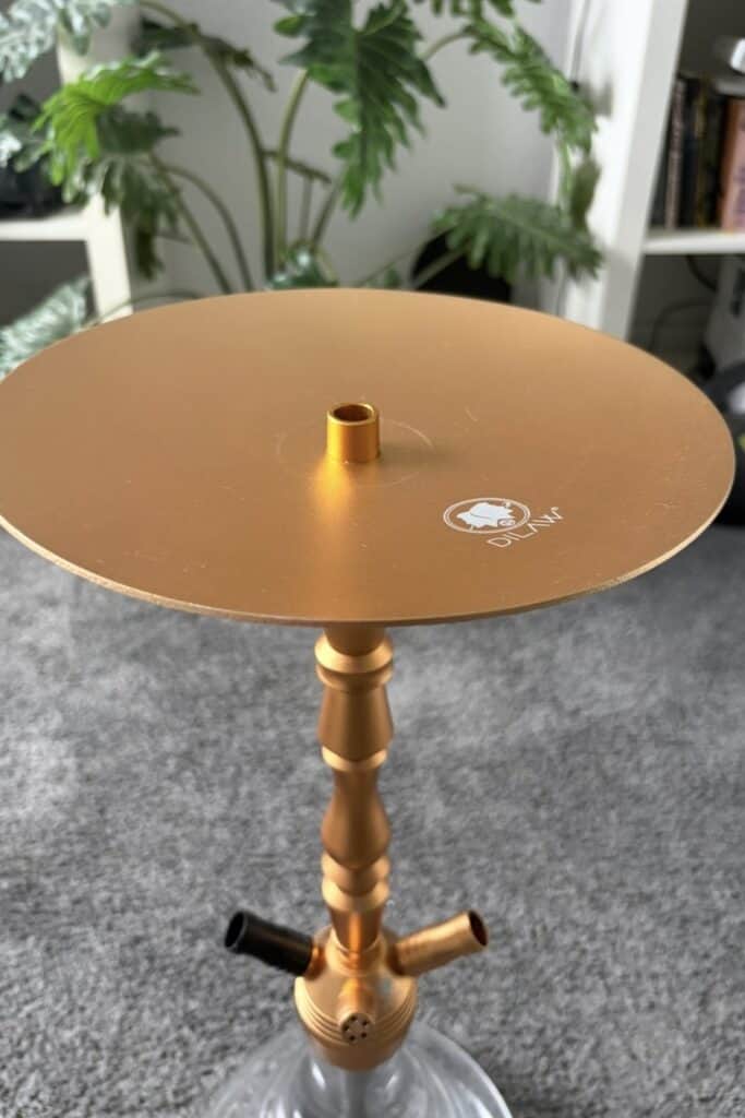 Goldene Shisha mit Glas-Schüssel und Metallständer, auf Teppichboden.