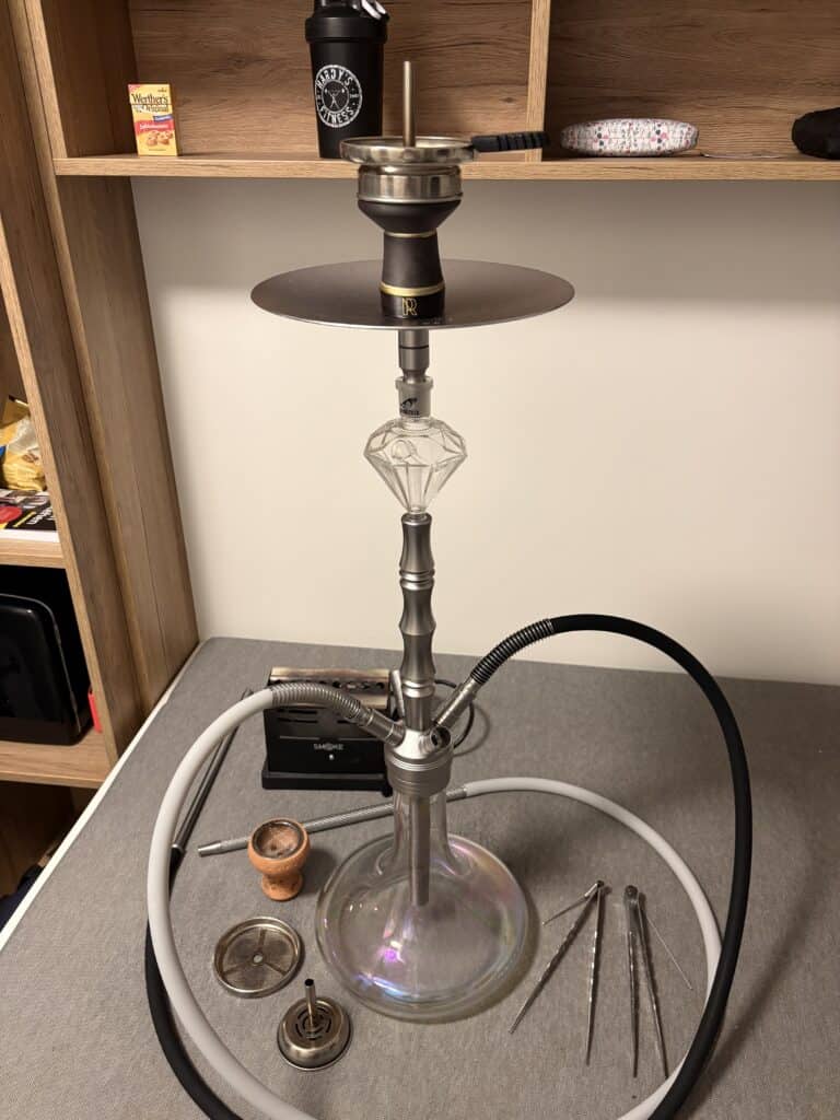 Rauchsäule mit Shisha, Tabak und Zubehör auf einem Tisch.