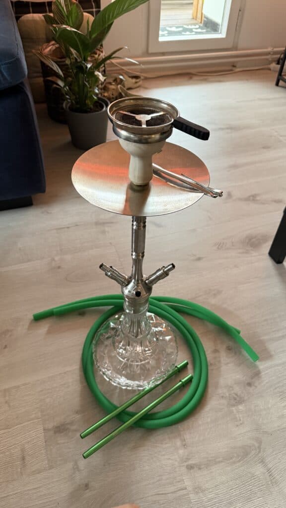 Shisha mit Glasbase, Schlauch und Kopf auf einem Tisch.