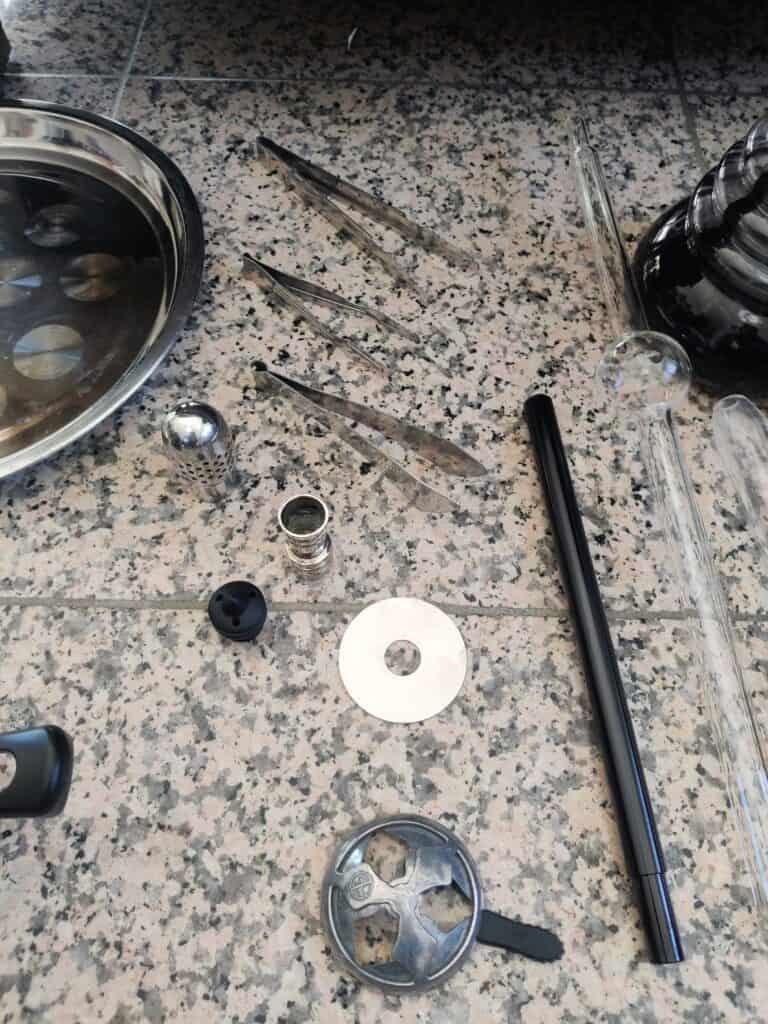 Verschiedene Shisha-Teile und Zubehör auf Steinboden verteilt.
