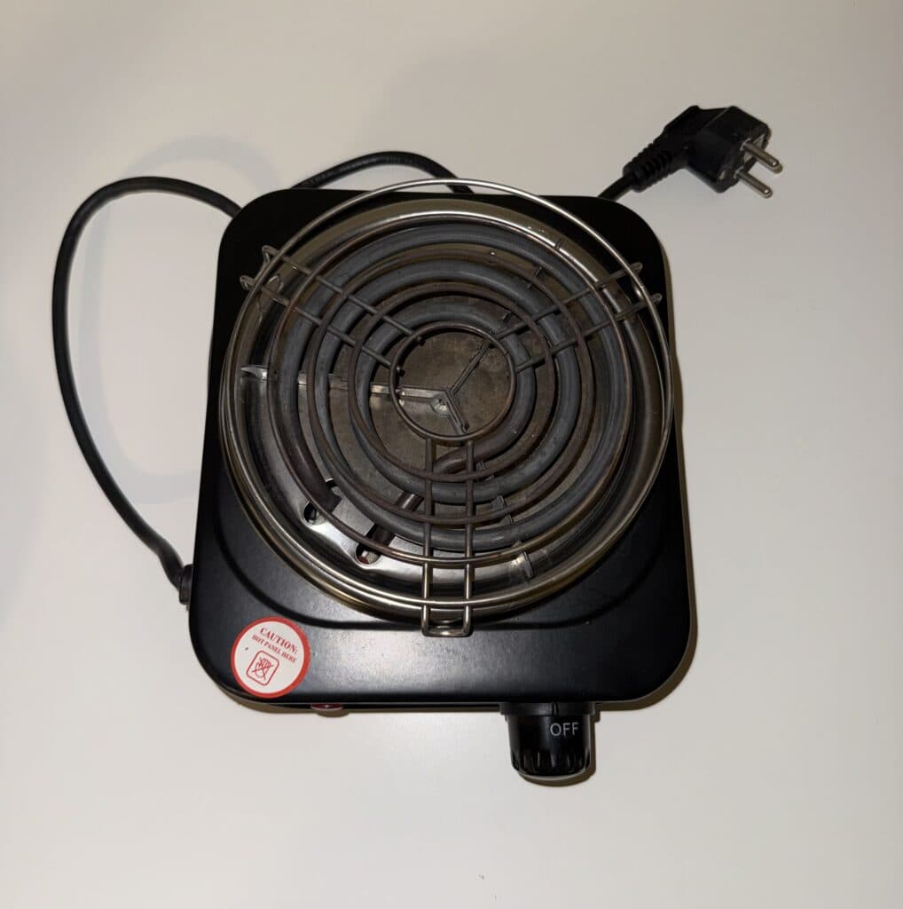 Kleine elektrische Kochplatte mit Gitter und Temperaturregler, ideal für Camping oder kleine Küchen.