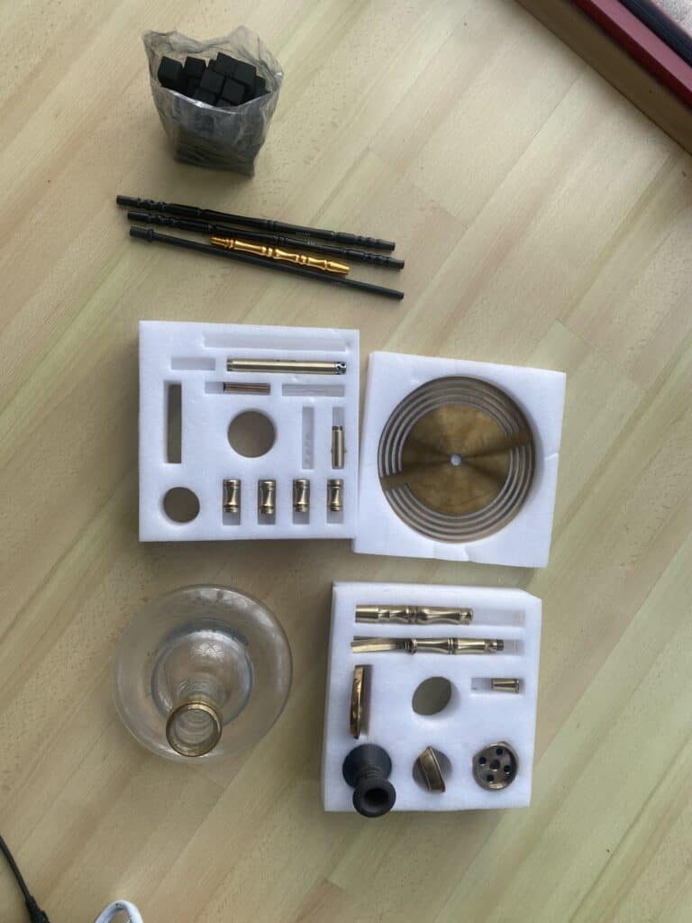 Zubehör für Shisha, inklusive Dichtungen, Schlauch und Ersatzteile, auf einer Holzoberfläche.