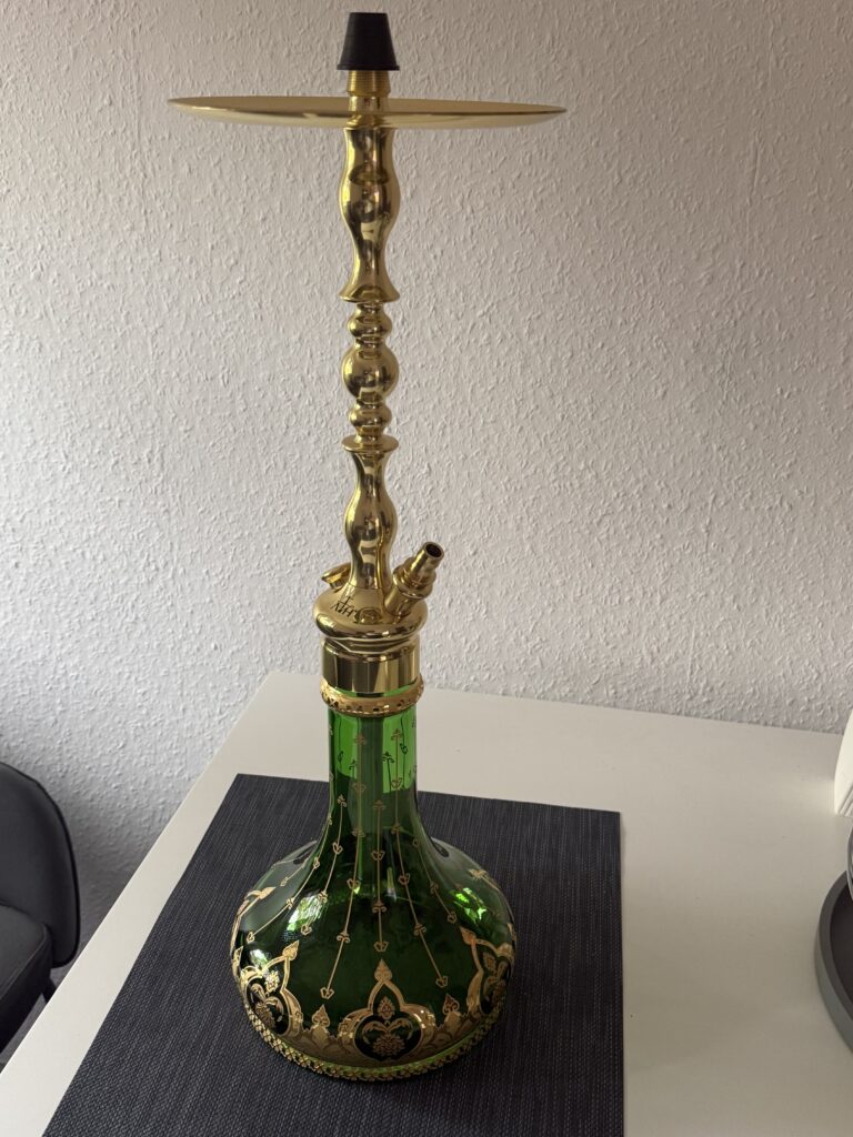 Shisha mit goldener Kopf und grünem Glas, auf einem Tisch.