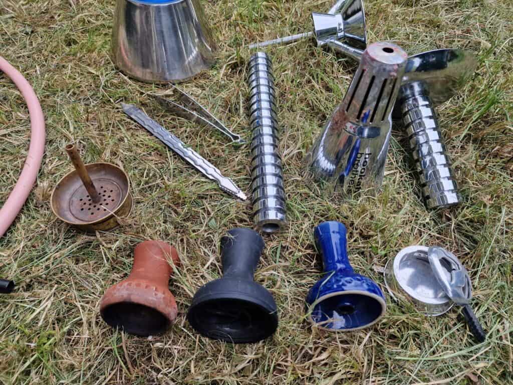 Verschiedene Grillzubehörteile, darunter Grillroste, Zangen und Kochutensilien, liegen auf dem Gras.