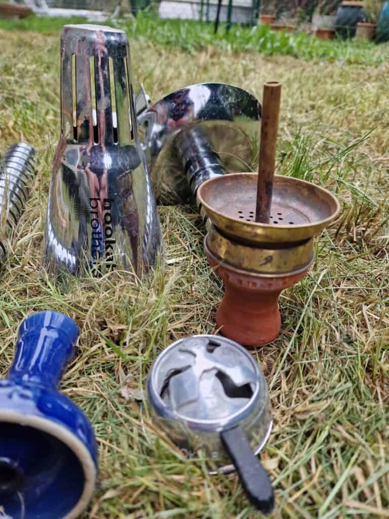 Verschiedene Metallteile und Zubehör für Shisha auf Gras im Garten.
