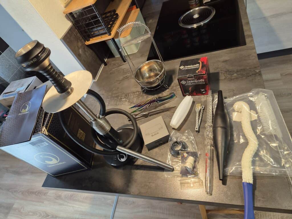Shisha mit Zubehör auf dunklem Tisch, inklusive Schlauch, Kohle und Ersatzteilen.