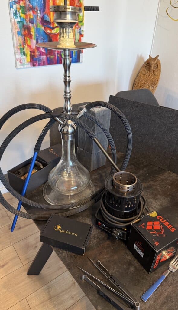 Rauchsäule mit Shisha, Tabak, Kohle und Zubehör auf Tisch.