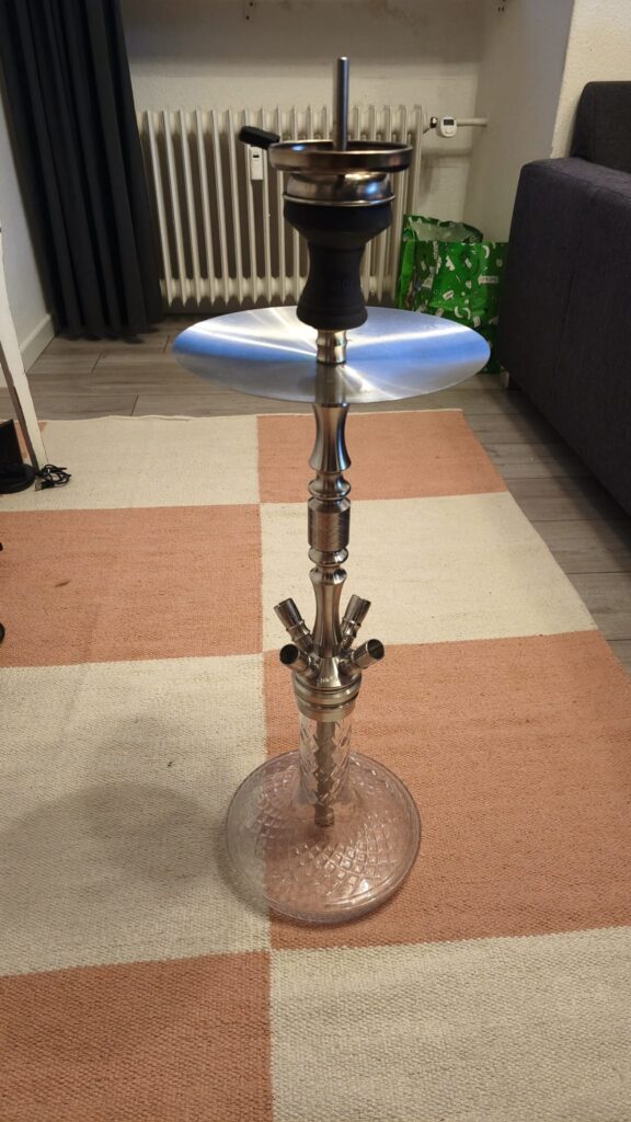 Shisha-Kopf mit Glasbowl und Metallstange, auf Teppichboden.