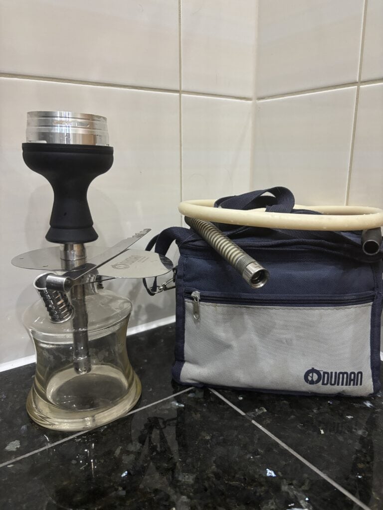 Shisha-Glasbowl mit Schlauch und Tasche auf Fliesenboden.