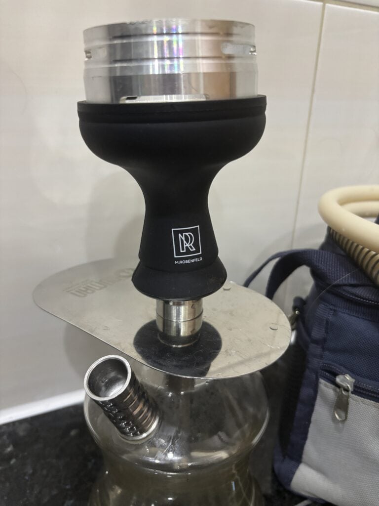 Shisha Glasbowl mit Adapter auf Metallplatte, neben Tasche.