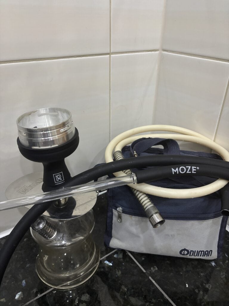 Shisha-Glasbowl mit Schlauch und Zubehör auf Fliesenboden.