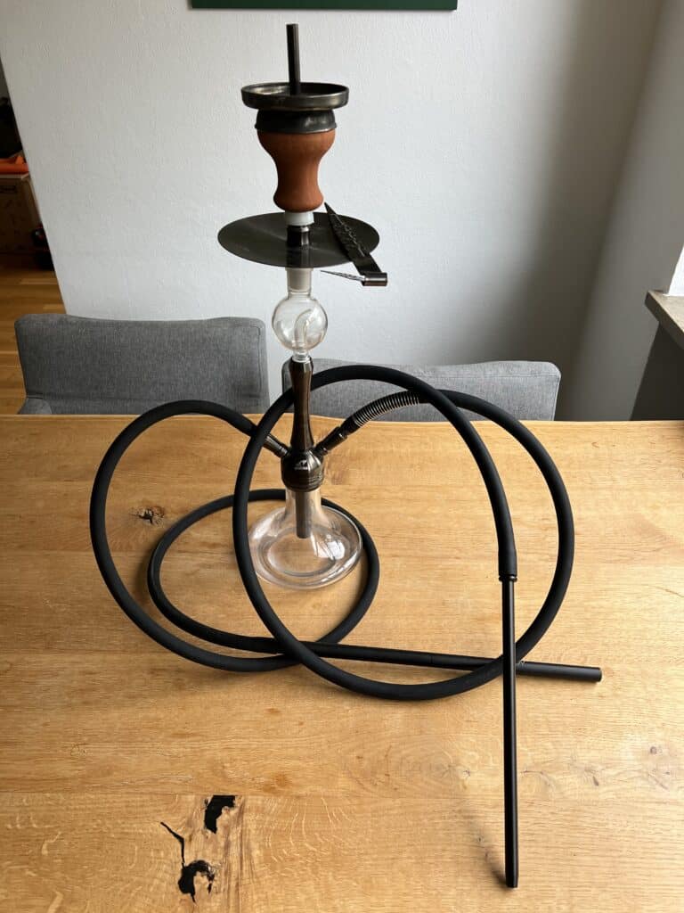 Shisha mit Glasbowl, Schlauch und Kopf auf Holztisch.