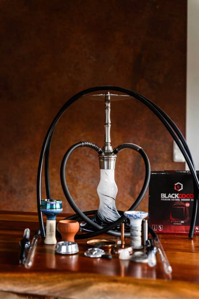 Moderne Shisha mit Glasbowl und Zubehör auf Holztablett.