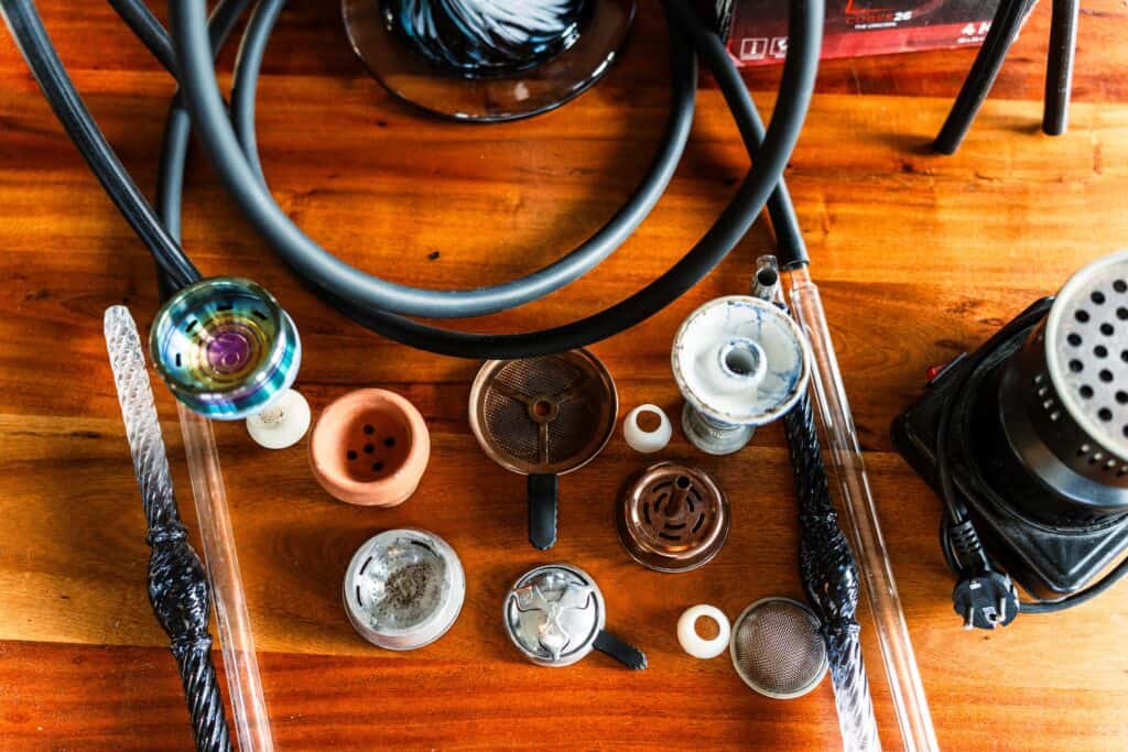 Verschiedene Shisha-Glasbowl, Schlauch und Zubehör auf Holz.
