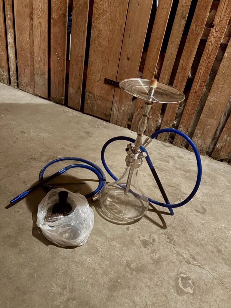 Shisha mit Glasbowl, Schlauch und Zubehör auf Betonboden.