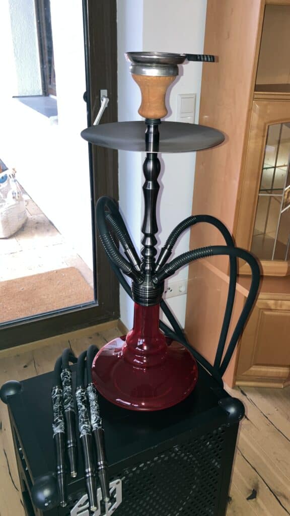 Shisha-Kopf mit Glasbowl und Schlauch, auf einem schwarzen Tisch.