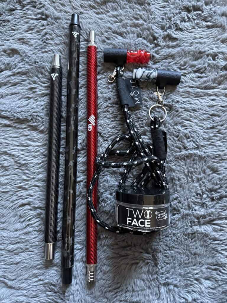 Verschiedene Shisha Zubehöre, inklusive Züge und Tasche, auf grauem Fellhintergrund.
