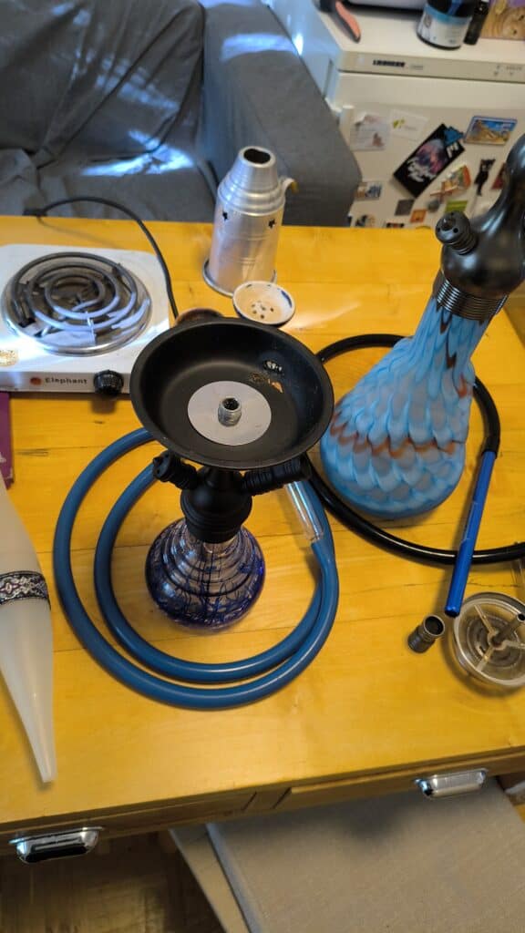 Shisha mit blauer Glasbowl, Heizplatte und Zubehör auf Holz.