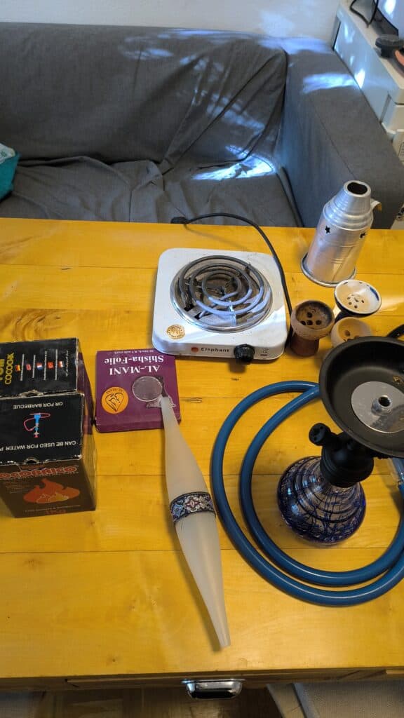 Shisha Zubehör mit Glasbowl, Schlauch und Heizgerät auf Tisch.