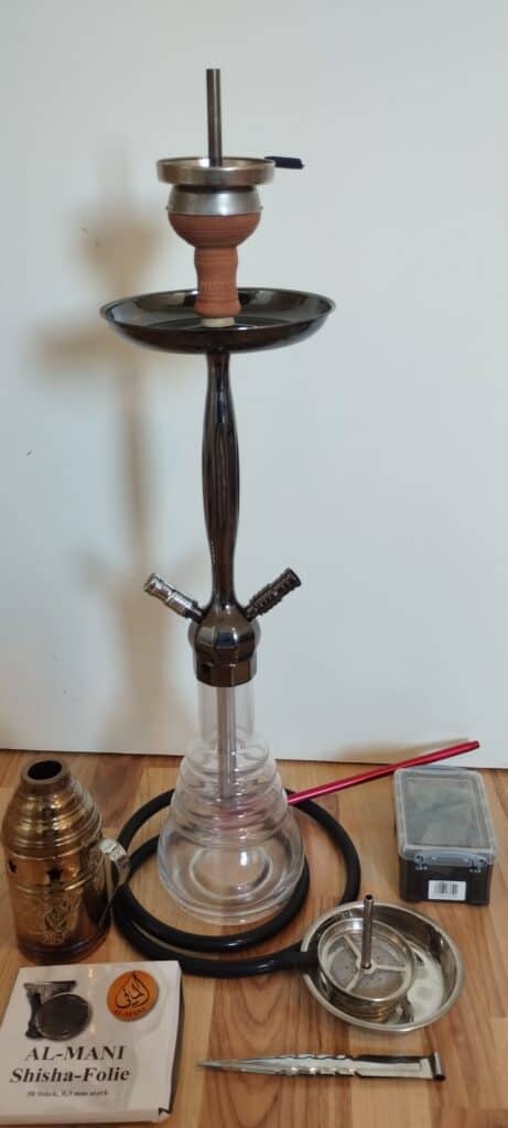 Shisha mit Glasbowl, Schlauch und Zubehör auf Tisch.
