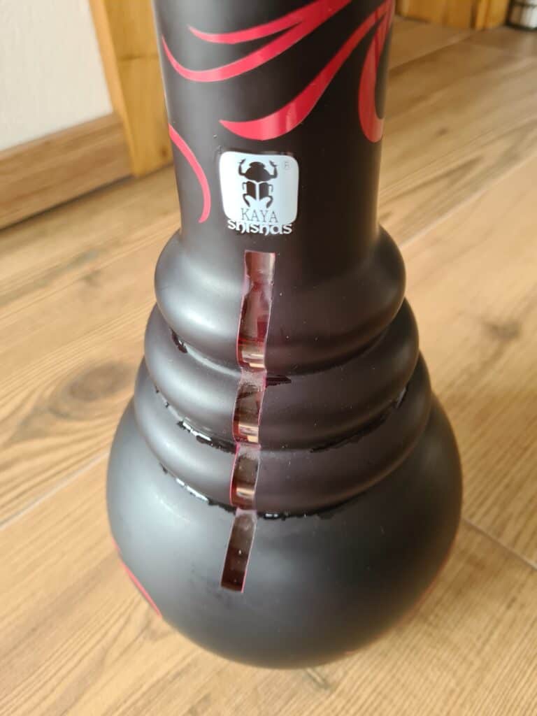 Schwarze Shisha mit roter Dekoration und Glasbowl, auf Holzboden.