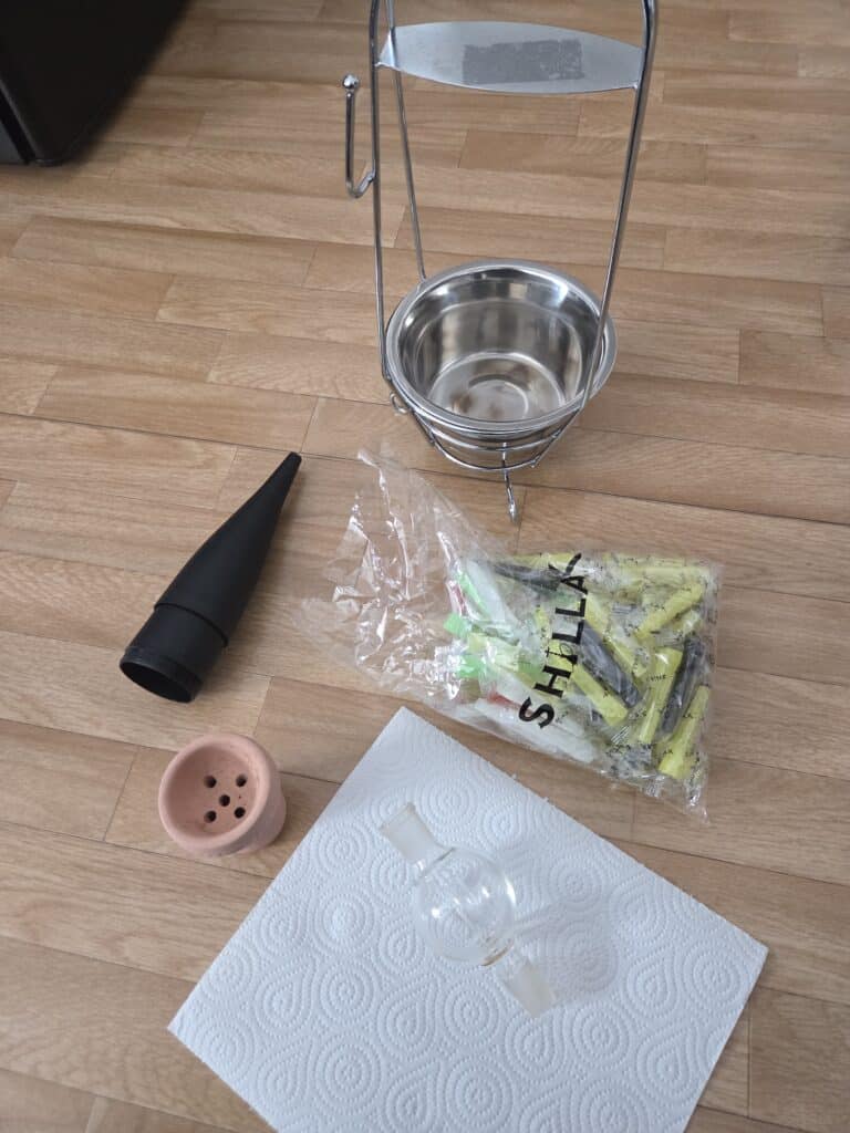 Shisha-Zubehör mit Glasbowl, Kohlezange, Tabakdose und Reinigungsbürste.