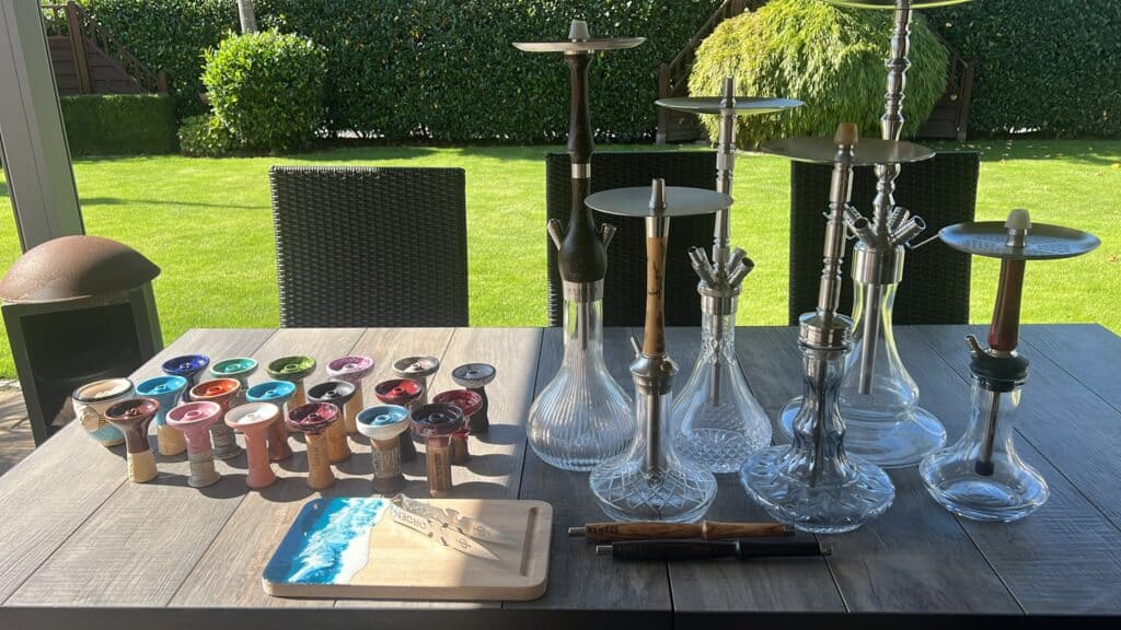 Verschiedene Glasbowl und Shisha-Zubehör auf Tisch im Garten.