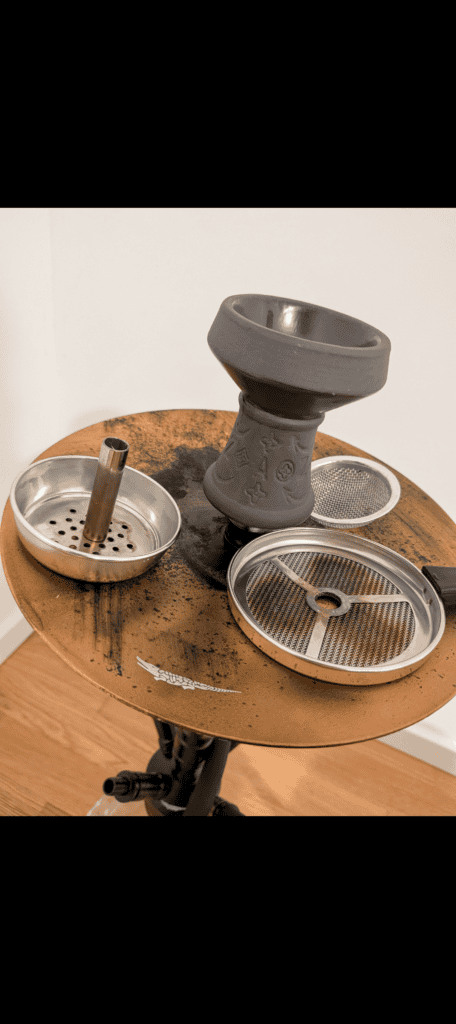 Shisha-Zubehör mit Glasbowl, Sieb und Kohlenhalter auf Holztablett.
