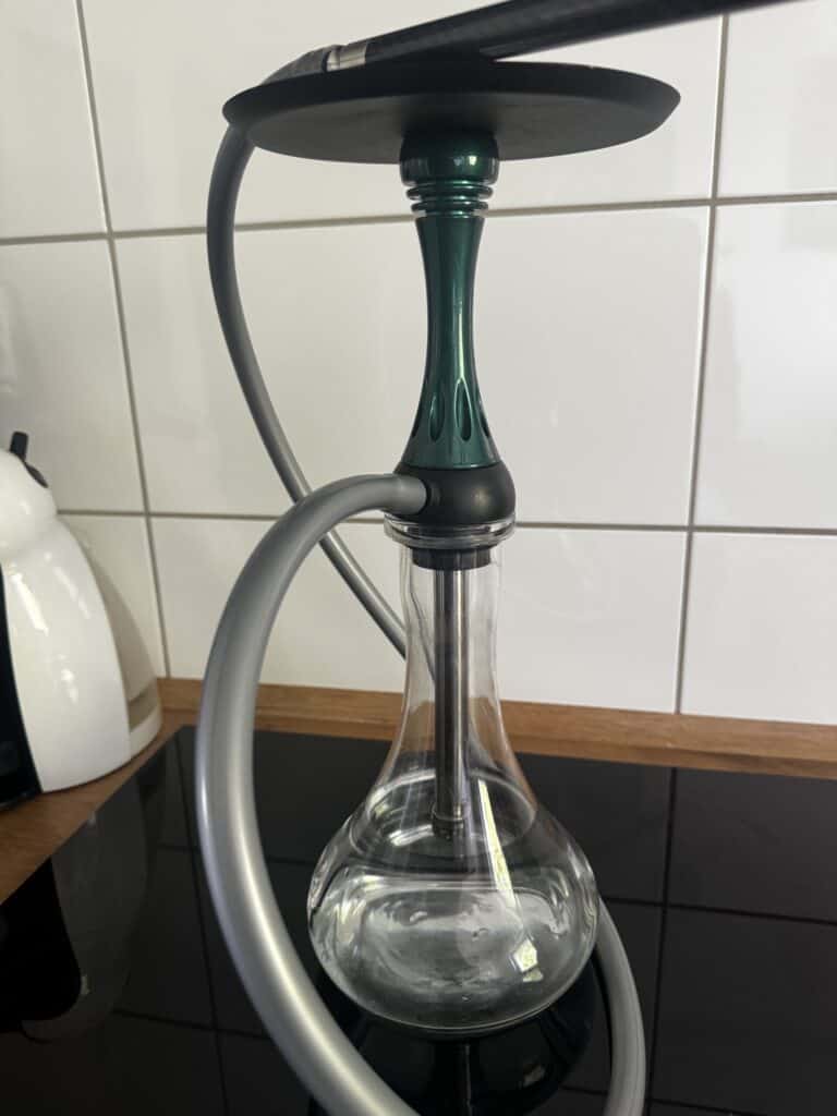 Shisha mit Glasbowl, Silikonschlauch und Metallaufsatz auf Tisch.