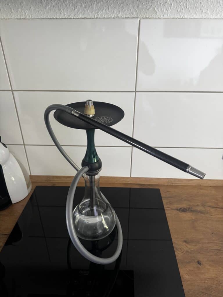 Shisha-Kopf mit schwarzem Schlauch und Glasbowl auf Holzplatte.