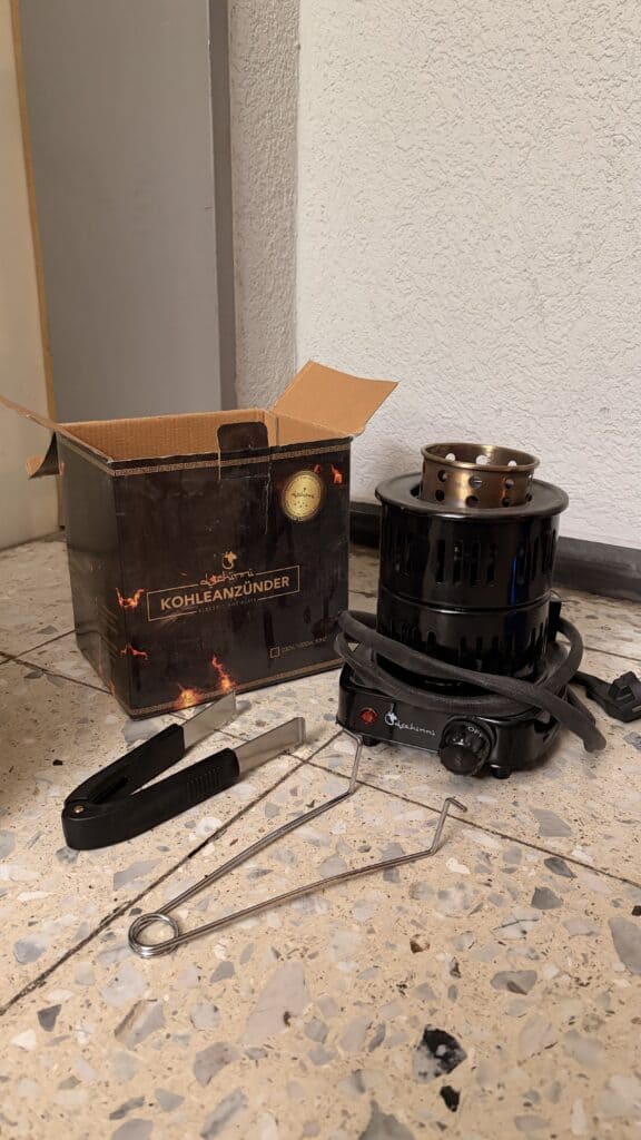 Kohleanzünder mit Metallzange und Glasbowl im Hintergrund.