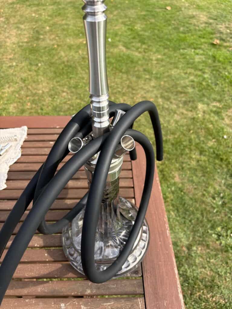 Moderne Shisha mit Glasbowl, Metallrohr und Schlauch auf Holztisch.