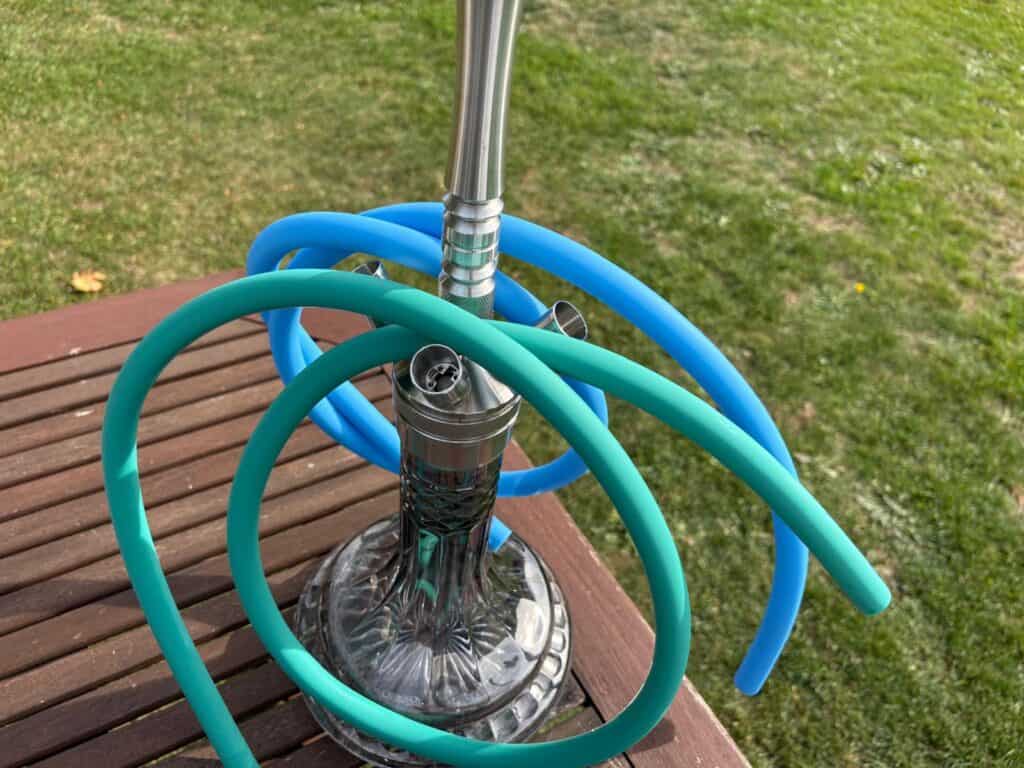 Shisha mit Glasbowl und flexiblen Schläuchen auf Holzbank im Garten.