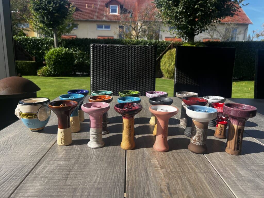 Vielfalt an Shisha-Glasbowl-Designs auf Tisch im Garten.