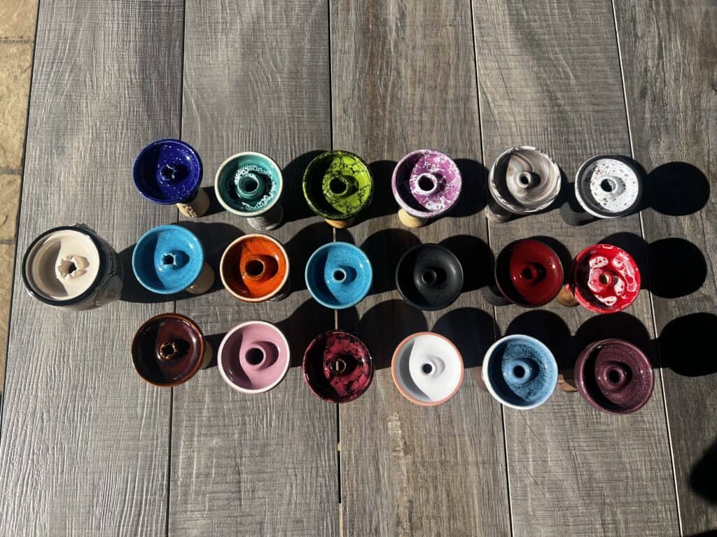 Bunte und schwarze Glasbowl-Varianten für Shisha, auf Holztisch arrangiert.