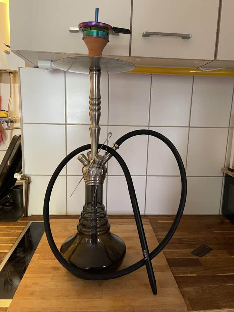 Shisha mit Glasbowl, Metallrohr und Silikonschlauch auf Holzplatte.