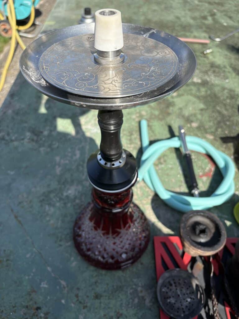 Shisha mit Glasbowl und Zubehör auf Außenfläche.