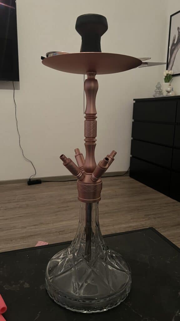 Shisha-Kopf mit Glasbowl und Zubehör, auf Tisch stehend.