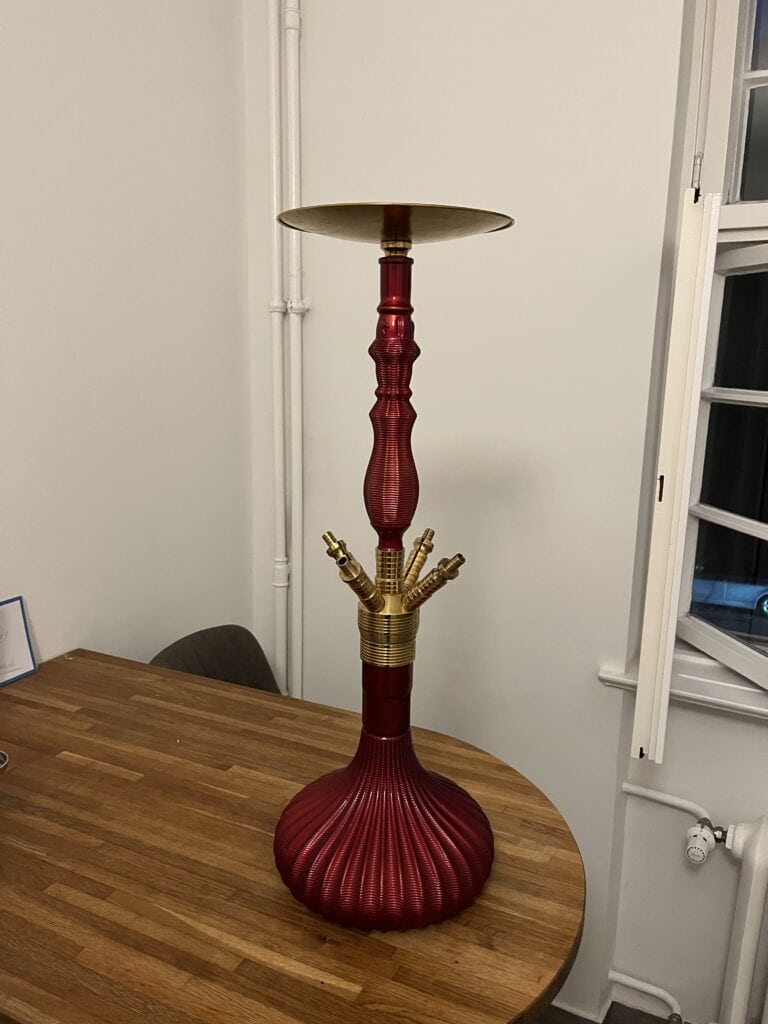 Roter Shisha-Kopf mit goldenen Anschlüssen auf Holztisch.