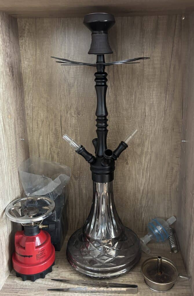 Schwarze Shisha mit Glasbowl und Zubehör im Holzregal.