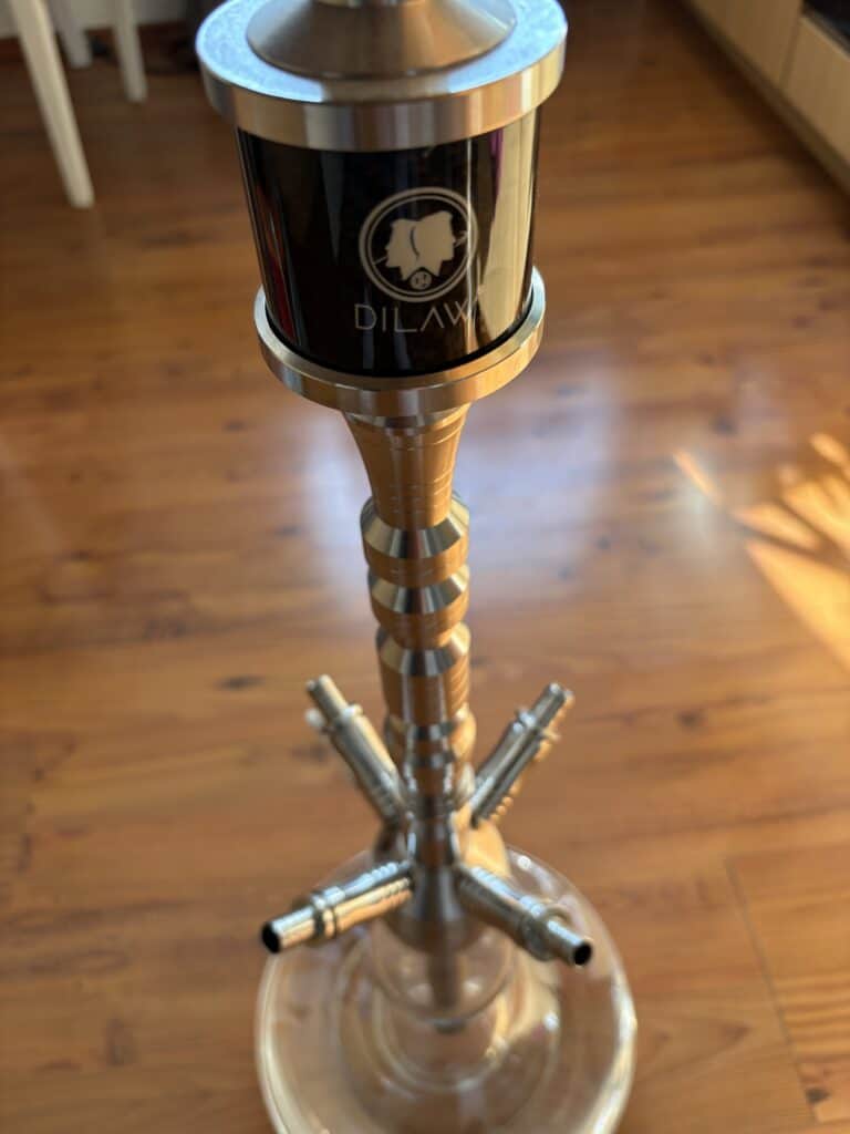 Shisha-Kopf mit Standfuß und Metallrohren, auf Holzboden.
