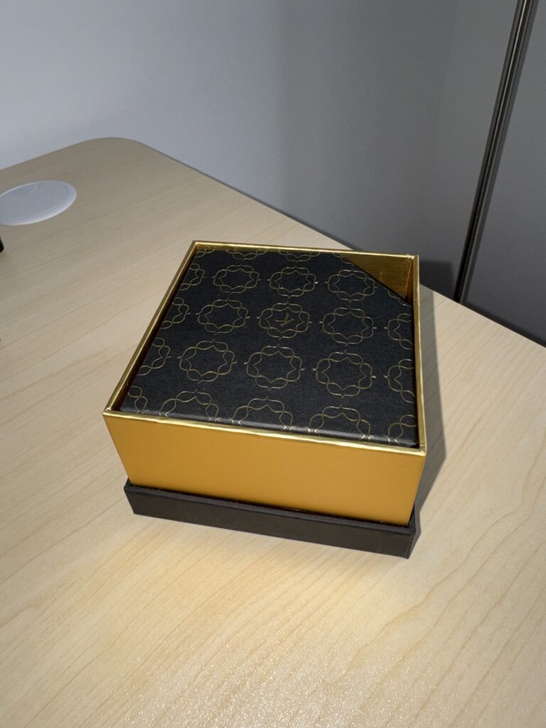 Schwarze und goldene Verpackung für Shisha-Zubehör auf Holztisch.