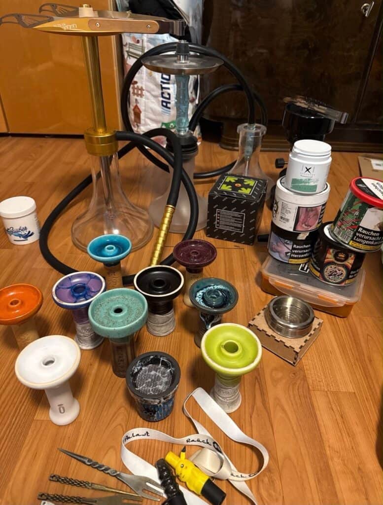 Verschiedene Shisha-Teile, Glasbowl, Tabakdosen und Zubehör auf Holztisch.