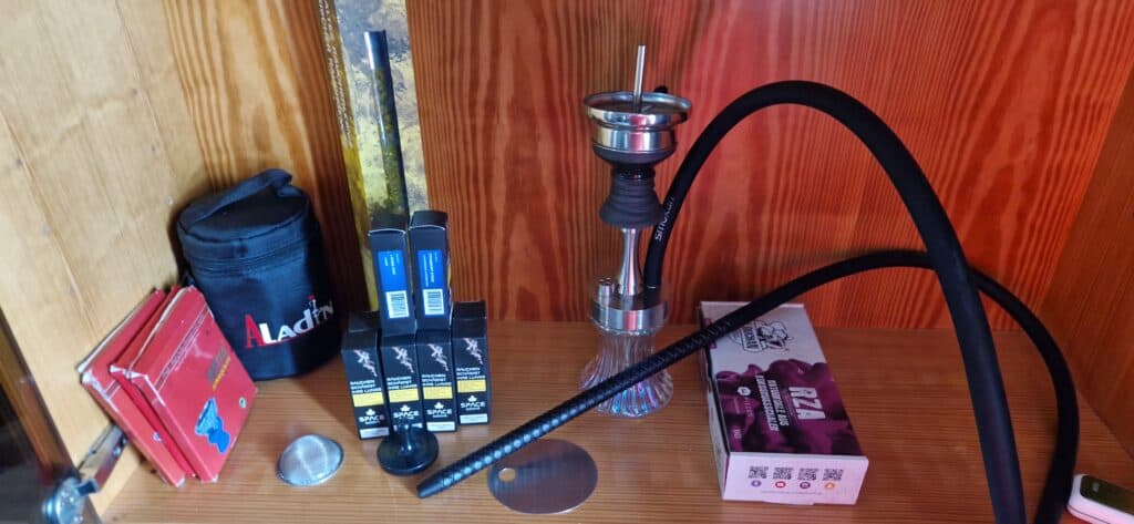 Shisha mit Glasbowl, Kohle, Zange und Zubehör auf Holz.