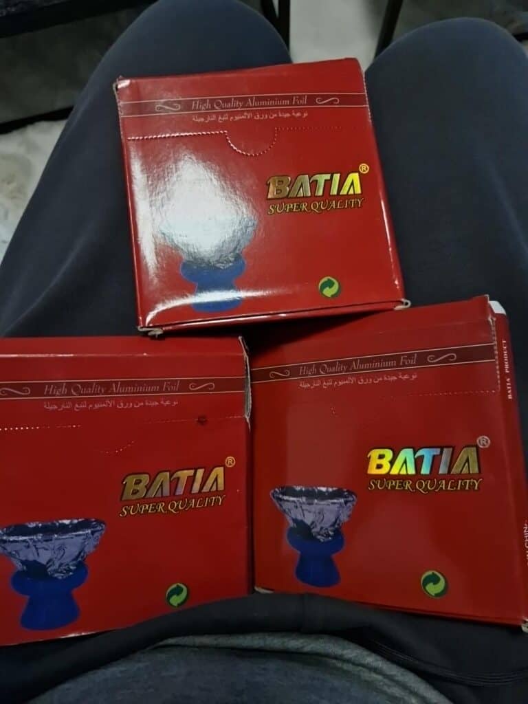Drei BATIA Aluminium Shisha Bowls in roter Verpackung auf den Beinen einer Person.