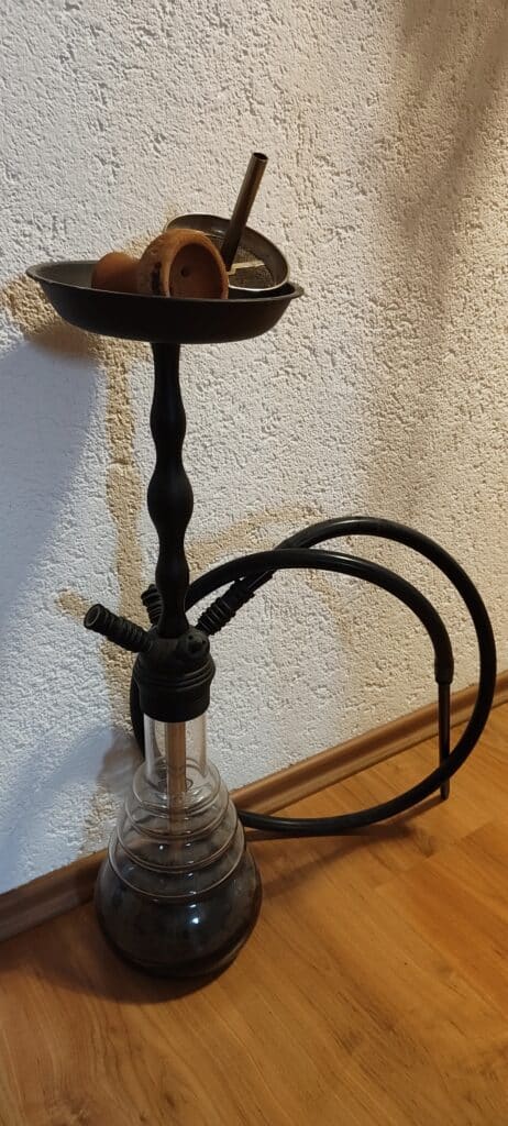 Shisha mit Glasbowl, Schlauch und Tabakhalter auf schwarzem Stand.