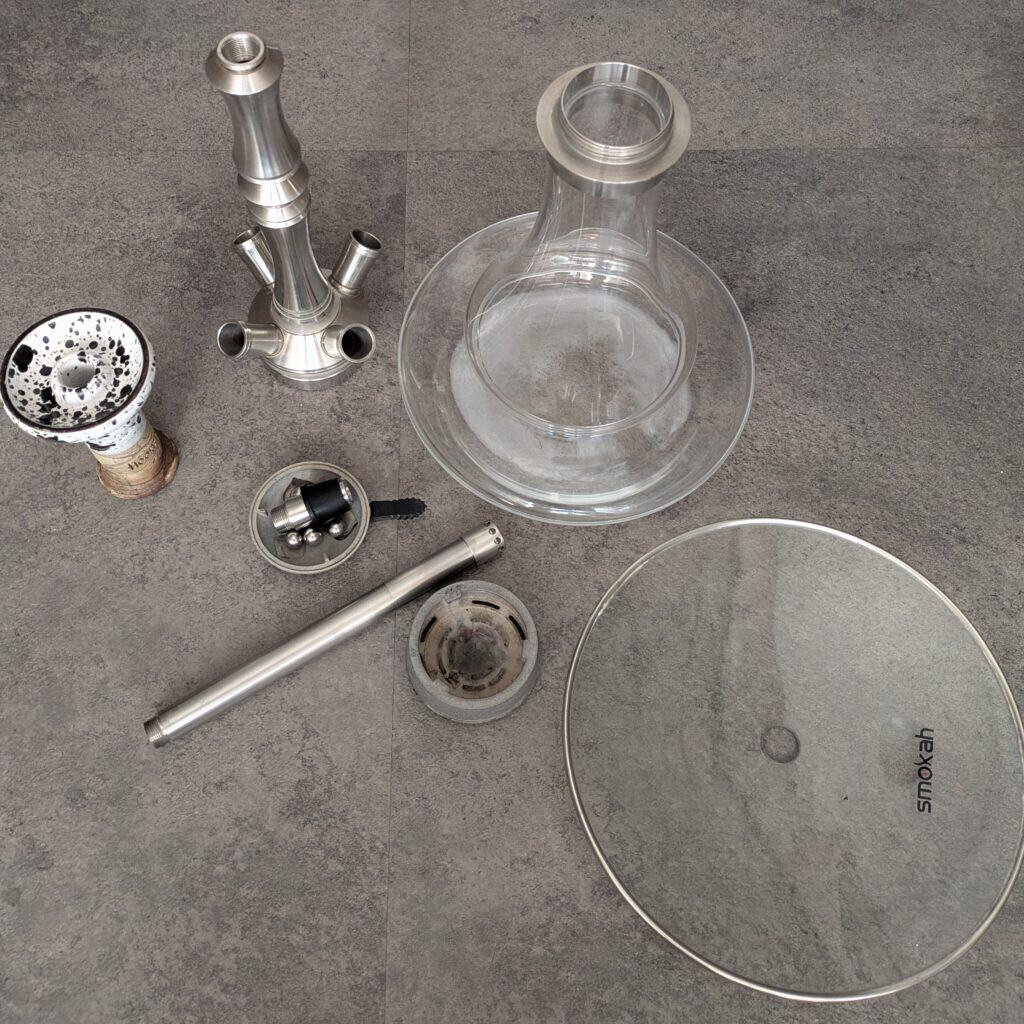 Verschiedene Shisha-Teile, inklusive Glasbowl und Metallkomponenten.