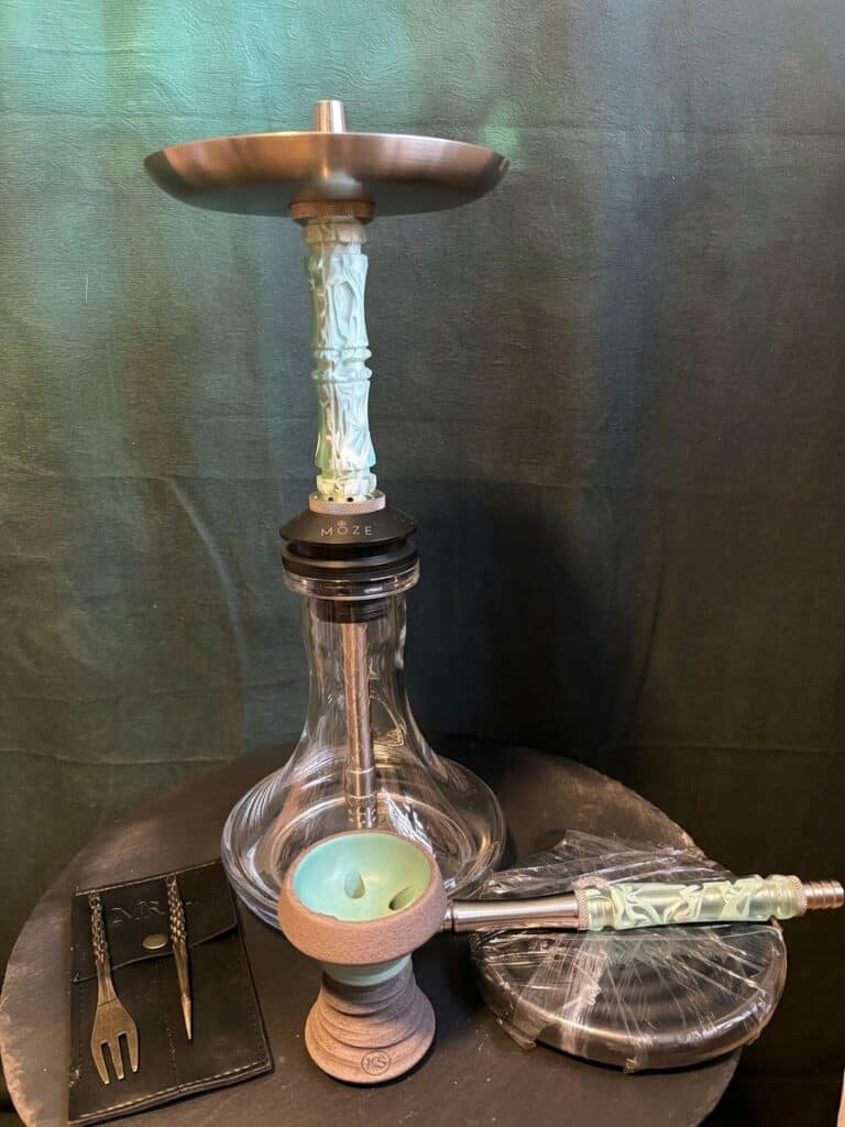 Shisha mit Glasbowl, Metallaufsatz und Zubehör auf schwarzem Hintergrund.