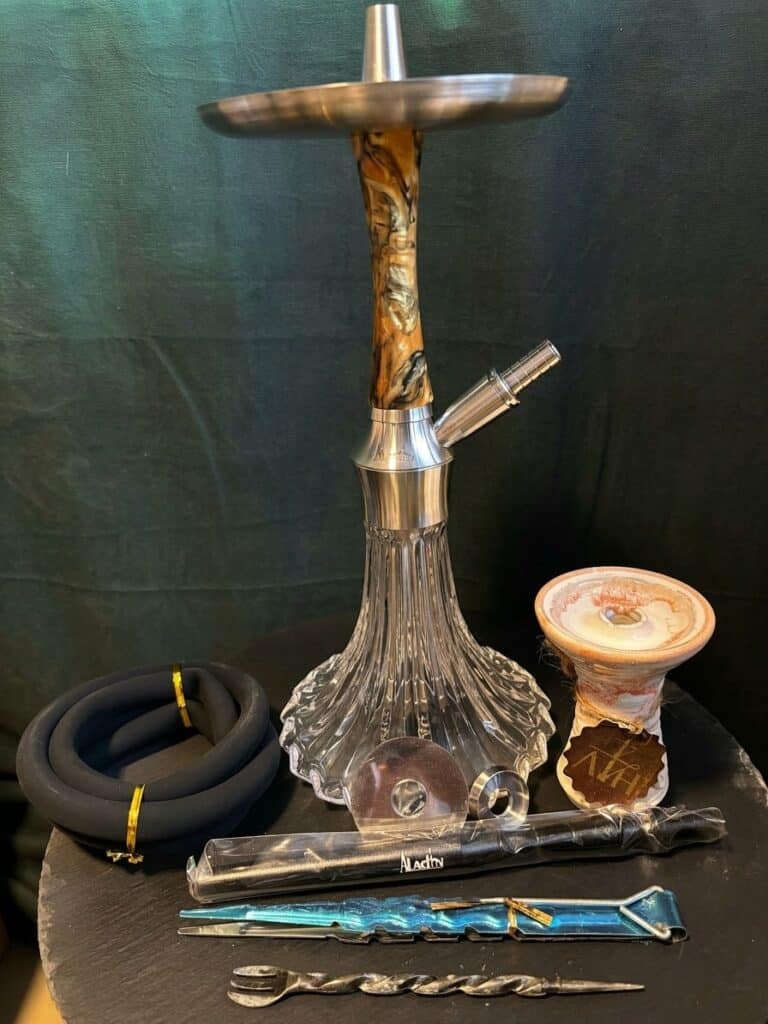 Shisha-Kopf mit Glasbowl, Schlauch und Zubehör auf schwarzem Tisch.