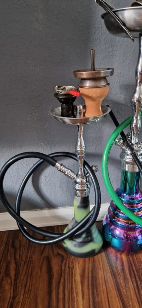 Shisha mit Glasbowl, Tonkopf und Schlauch auf Holztisch.